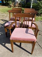 Front view of the set showing four chairs without armrests and one chair with armrests, all with pink upholstered seats.