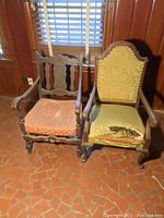 Two solid wood antique chairs, one with an orange patterned seat cushion and carved back, the other with a green high upholstered back and armrests, both needing refurbishment and repair
