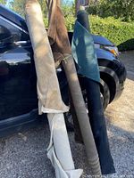Three rolls of fabric leaning against a car, colors beige, brown, and blue, showing size and appearance.