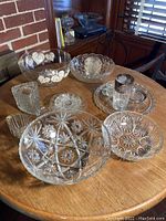 Overview of all cut and depression glass bowls, plates, and cups arranged on a wooden table.