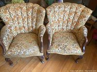 Pair of vintage wing back chairs with floral fabric upholstery, showing full front and side view to capture overall condition, fabric pattern, and wooden legs.