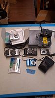 Wide shot showing full lot on table including cameras, boxes, manuals, battery, and camera case