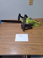 Side view of the Poulan Wildthing 2375 chainsaw on a wood table showing the chain, blade, and body colors.