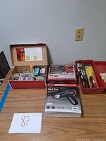 Photo of the full lot including boxed jigsaw, heat gun, tool tray, and other accessories on a table with lot number.