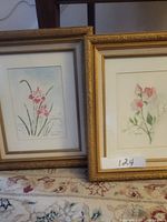 Two framed watercolor paintings by Myrtle Carlson placed on carpet. Both paintings show flowers and have gold ornate frames with mats.