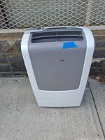 Front view of the white and grey Frigidaire portable air conditioner with the remote control on top.