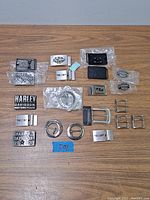 Overview of all belt buckles and accessories laid out on wood surface, showing variety of sizes and logos.