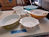 Wide view of the lot showing various Pyrex bowls including nesting Cinderella shapes, glass lid casserole, and colorful patterned bowls placed on a table
