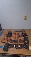 Photo showing assorted leather holsters, grips, magazine pouches, and a decorative leather belt laid out on a table.