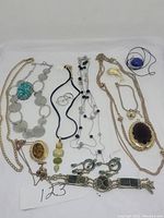 Mixed costume jewelry including necklaces, bracelets, earrings, and chains arranged on white background.