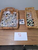Wide view of two woven baskets containing multiple small bottles of oil diffuser fragrance oils in plastic bags, with a pack of matches placed between them on a table.