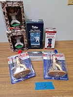 Front view of Brad Lidge bobblehead figurines in boxes, Jim Thome limited edition figurine box, Phillies solar-powered Liberty Bell box, and two Starting Lineup Phillies baseball figurines in packaging on table.