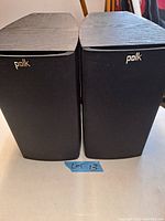 Front view of Polk speakers with front grills on, showing brand logo.