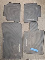 Set of four Porsche rubber floor mats laid out on carpet, showing top front side with Porsche logo visible