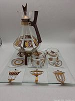 Full frontal view of the coffee set including the carafe, warmer, creamer, sugar bowl, and serving plate decorated with gold and brown retro atomic patterns.