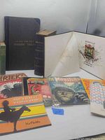 Lot of vintage ephemera including hardback books (4, 5 & 7 Per Cent Interest Tables, Ladies Repository), colorful magazines (Shriek!, Monster World), mobster comics, Doll News publications, and booklets Oklahoma and KeMolta laid out showing cover art and interior page of A.O.U.W. Camden Lodge Memorial book.