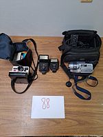 Full lot showing Polaroid camera and case, two flash units, Sony Handycam and its carrying case on wood surface.