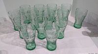 Front view of 14 green Coca Cola glasses arranged together, showing their size and shape.