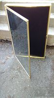 Gold tone metal framed display case opened showing black velvet interior backing and glass door.