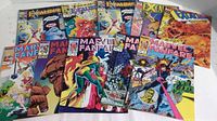 Ten comic books laid out on a white surface, including series Excalibur and Marvel Fanfare. Covers show various Marvel characters and colorful scenes.