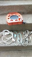 Orange Noma Cord Caddy reel plus three extension cords lying on concrete steps