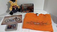 Photo of lot with plush pig, boxed die cast motorcycle, playing cards tins, tin sign, and orange long sleeved T-shirt