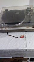 Turntable with closed dust cover and RCA cables visible, front view.