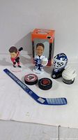Photo showing Curtis Joseph and Seabrook bobbleheads, two helmets, two pucks, and a mini hockey stick in front of box