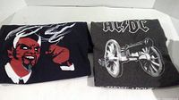 Two black t-shirts folded, one with graphic of horned figure with flames and the other an ACDC shirt with cannon graphic.