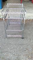 Front angled view of the stainless steel shelving unit showing two sliding wire mesh drawers, caster wheels, and missing plastic foot on one leg.