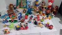 Photo showing a large assortment of toys and figures including Disney and Sesame Street characters laid out on a table.