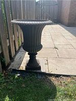 Side view of weathered metal urn planter showing fluted vertical lines and decorative rim.