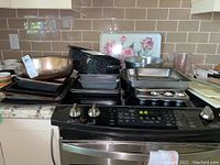 View of kitchen stove with stacked assortment of baking pans, sheets, cups and pans.