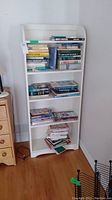 Full view of white painted wood bookcase with books on the shelves, showing size and condition.