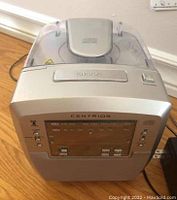 Front view of Centrios CD clock radio showing control buttons, display screen, and speaker area.