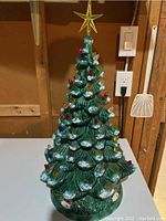 Front view of the vintage ceramic Christmas tree with colorful bulbs and gold star topper on white table against wooden wall.