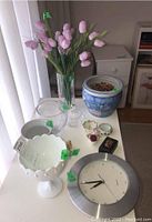 Overview photo of lot items showing Asian ceramic vase, glass vases including one with faux tulips, decorative bowls, miniature china, wooden box, and round silver wall clock.