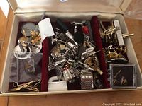 Full view of the jewellery box showing multiple metal cufflinks and tie pins arranged in velvet compartments.