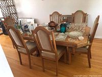 Wide shot of six oak dining chairs set around a wooden dining table with glassware on top. Shows upholstery on seats and backs, with two armrest chairs at ends.