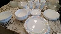 Corelle dinner plates, side plates, salad plates, bowls, coffee cups arranged on table with granite surface