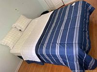 Photo of fully assembled double bed with mattress, plaid bedding and blue striped comforter, showing side and corner of bed setup in bedroom.