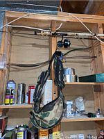 Two fishing rods with reels mounted on a wooden wall panel and a camouflage fishing tackle sack hanging below.