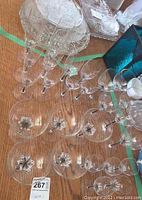 Photo showing multiple clear glasses arranged on a wooden surface, highlighting their black accented stems and bases, including several champagne, flute, and other types.