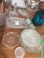 Photo showing various cut glass platters, bowls, and a decorative bottle with metal lid on a wooden table.