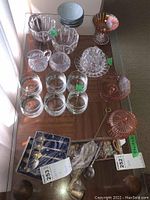 Overview of various glassware including whiskey glasses, bowls, pink depression glass, silver plated spoons in box, and small cookware items.