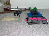 Photo showing pairs of ankle weights, multiple hand weights, wooden baseball bat, black charger, zip ties on carpeted floor.