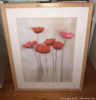 Close-up photo of the flower print in a wooden frame showing orange and pink flowers with thin black stems on a neutral background.