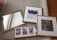 Four items laid on a textile surface including three wood framed prints with white mats and a metallic framed mirror