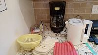 View of Black and Decker coffee maker, Russell Hobbs electric kettle, colander, oven mitts and cloth arranged on granite countertop