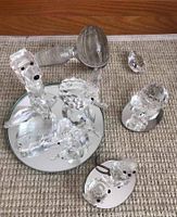 Overview of five Swarovski crystal animal figurines, showing swan, dog, cat and smaller animals on mirror plates. Swan, dog, and cat appear damaged. Loose glass stopper and chandelier crystal in background.